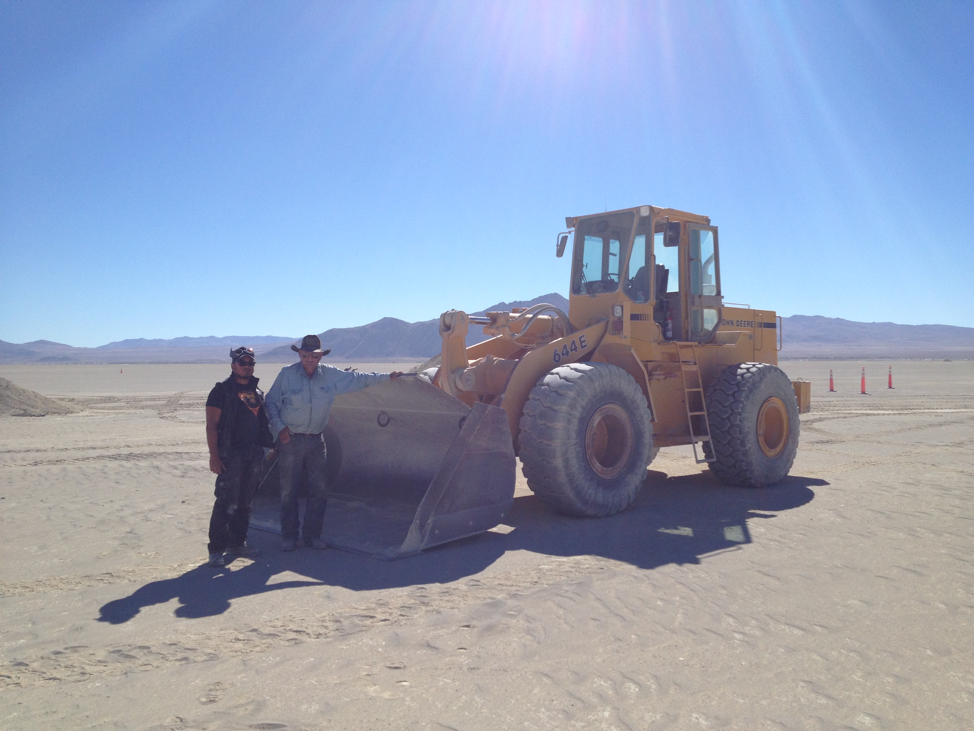Stuart from Gerlach (standing on the right, with Resto boss D.A.) works with Willie Courtney to use his heavy equipment to deal with the decomposed granite generated by Burning Man's large burns. Decomposed granite, or DG, is local to the area, and was suggested by the BLM as a heat-absorbing way to protect the playa from burn scars. DPW pulls the MOOP and metal scraps out of the cinders; the DG gets scooped up, cleaned, and reused.