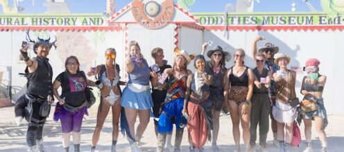 2023 Black Rock City sticker designers hold up their stickers in front of Media Mecca