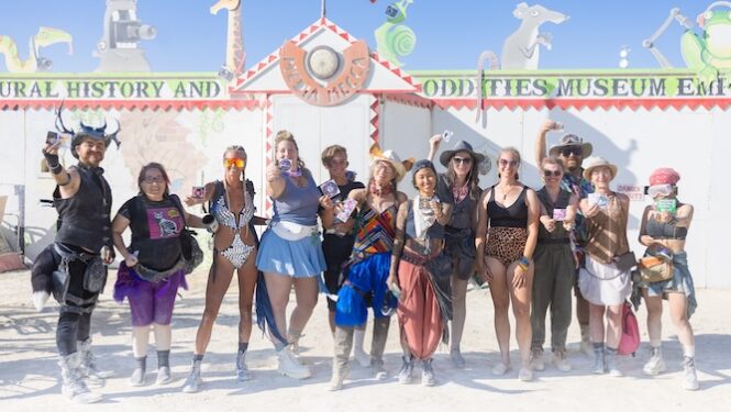 2023 Black Rock City sticker designers hold up their stickers in front of Media Mecca