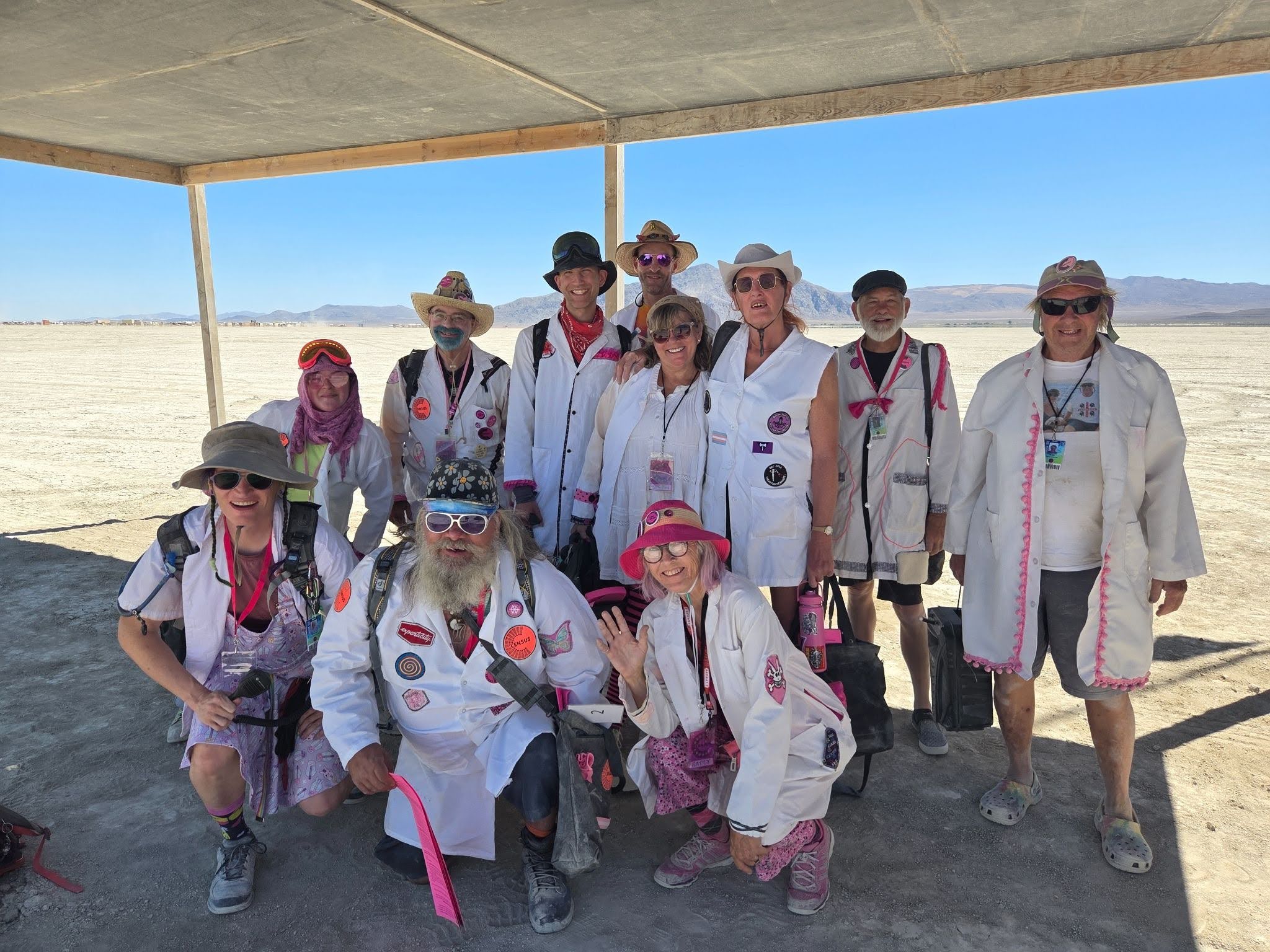 Census volunteers in lab coats pose under a canvas and wood shade structure.