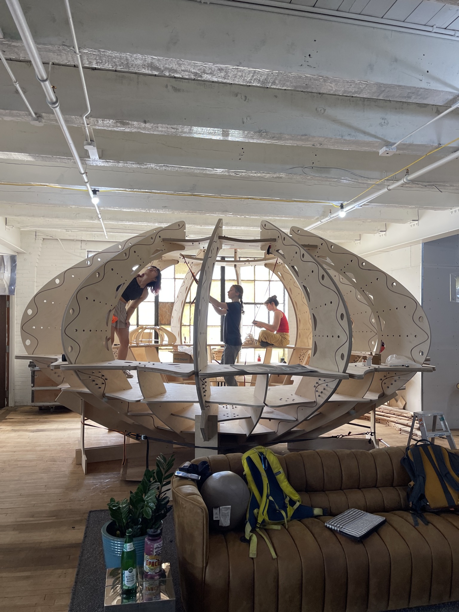 an oval sculpture made of wood in sharp focus in with people building something in the background.